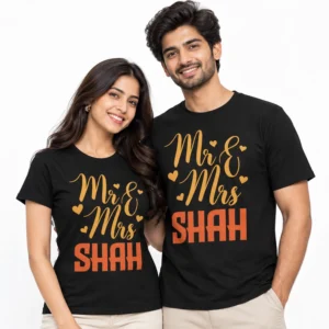 Indian couple wearing matching black personalized Mr. & Mrs. Shah T-shirts with golden script lettering, decorative heart motifs, and bold orange SHAH surname prints.
