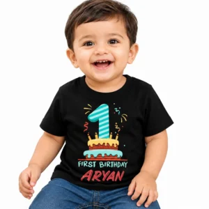 Smiling toddler wearing a black personalized 1st birthday kids t-shirt with colorful number 1 cake design and the name Aryan on a clean white background.