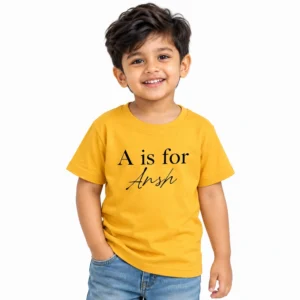 Smiling Indian boy wearing a yellow personalized kids T-shirt printed with the words A is for in black serif lettering and the name Ansh in black cursive script below.