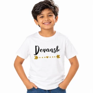 Smiling Indian boy wearing a white personalized kids T-shirt with the name Devansh in bold black cursive lettering and a decorative gold heart, dots and arrow motif underneath.