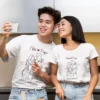 Couple wearing matching personalized T-shirts with custom names and date featuring minimal line art design while taking a selfie together