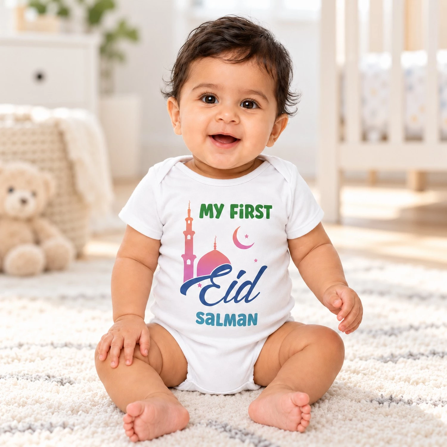Smiling baby wearing a white personalized First Eid romper with the name Salman while sitting in a bright neutral nursery.