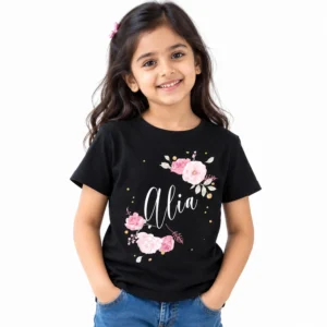 Smiling young girl wearing a black personalized T-shirt featuring the name Alia in large white cursive lettering surrounded by pink roses, pale leaves, and small gold dot accents.
