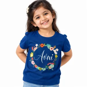 Smiling young girl wearing a royal blue personalized kids T-shirt featuring the name Avni in white cursive lettering inside a circular wreath of colorful pink, orange, yellow, and teal flowers.