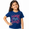 Smiling Indian girl wearing a royal blue personalized kids T-shirt featuring the name Nisha in white cursive lettering surrounded by bright pink and red heart graphics.