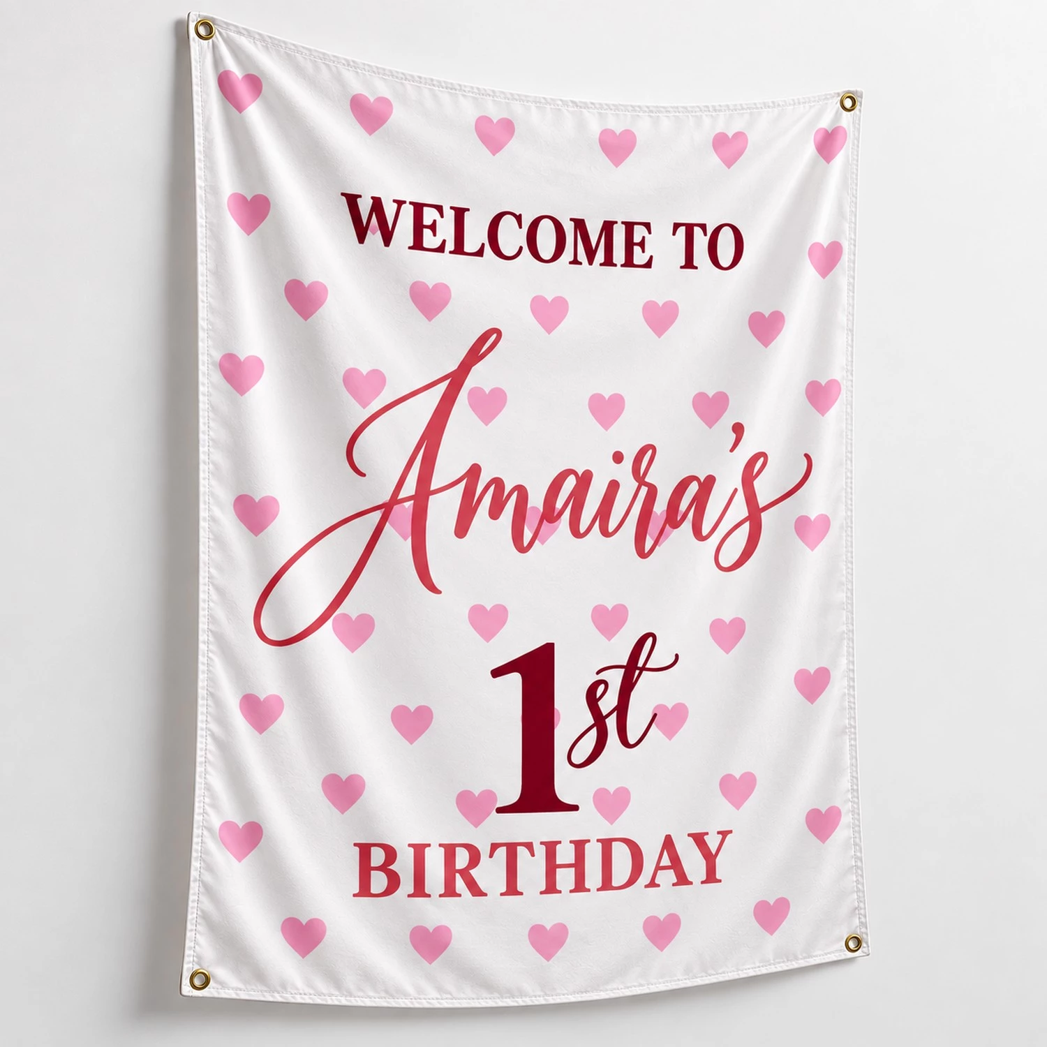 Personalized kids birthday tapestry banner with Amaira’s 1st birthday design, pink hearts, burgundy lettering, white fabric and four corner grommets.