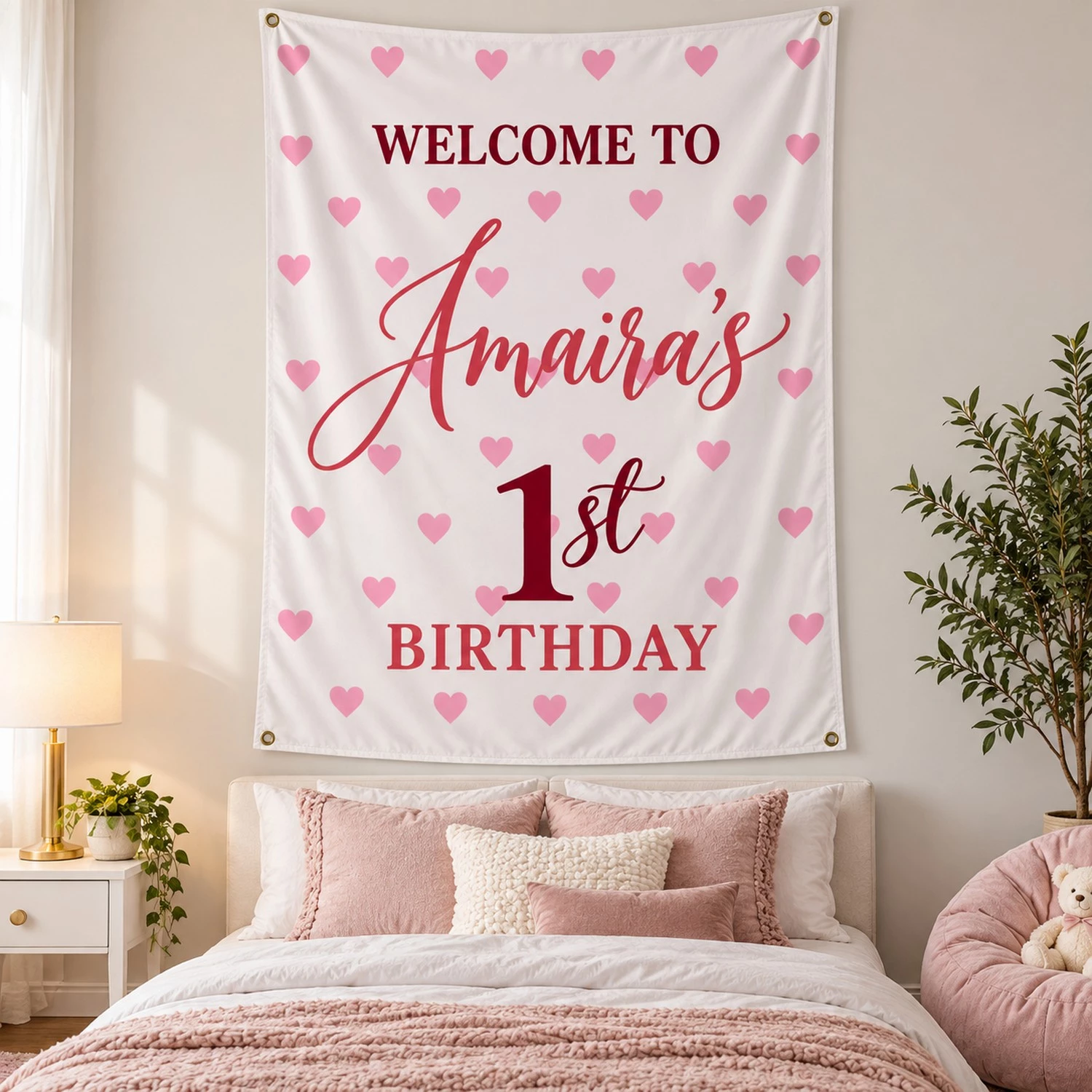 Large personalized kids birthday tapestry banner with Amaira’s 1st birthday design displayed above a bed in a pink and neutral bedroom.