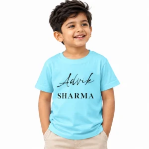 Smiling young Indian boy wearing a sky blue personalized kids T-shirt featuring the name Advik in black cursive lettering and SHARMA in uppercase serif text.
