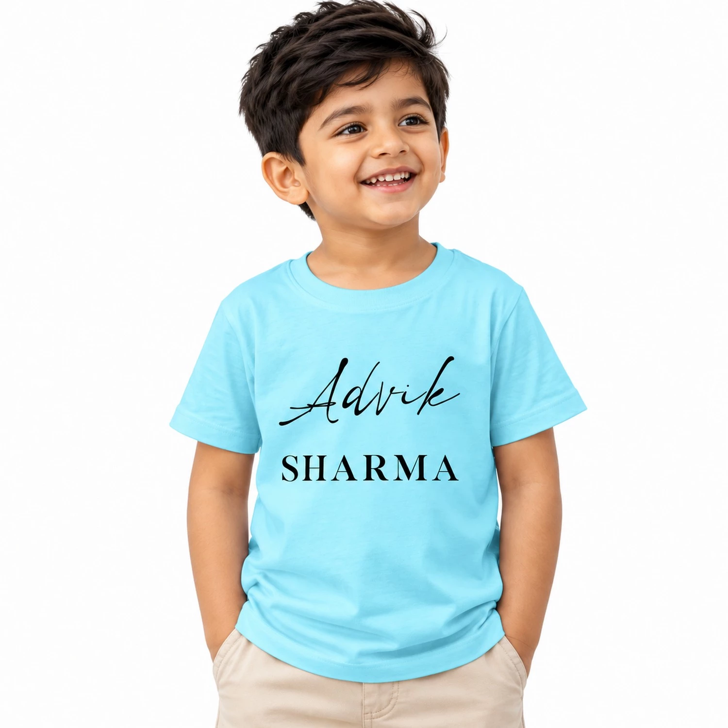 Smiling young Indian boy wearing a sky blue personalized kids T-shirt featuring the name Advik in black cursive lettering and SHARMA in uppercase serif text.