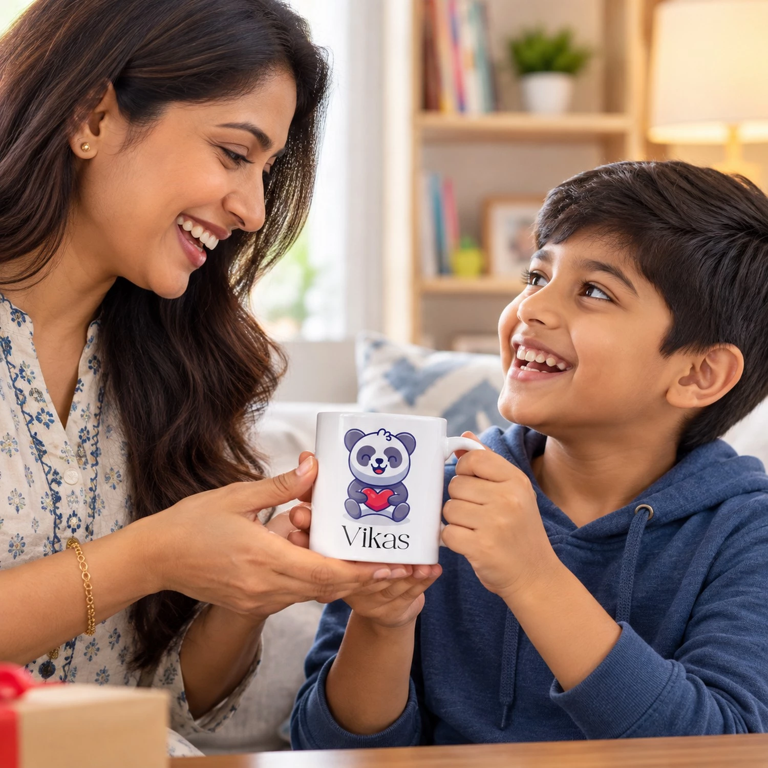 Mother and young boy smiling together while holding a personalized panda mug with a red heart and the name Vikas.