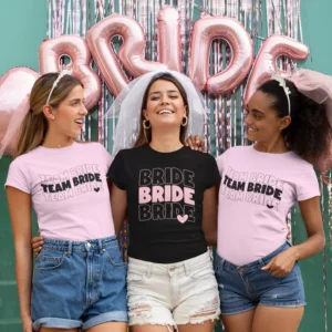 Three women wearing matching bride and team bride t-shirts at a bachelorette party celebration with decorative backdrop