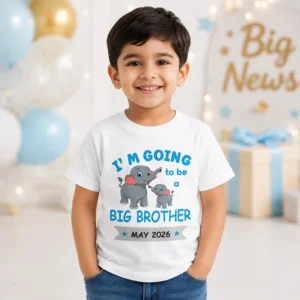 Smiling young boy wearing a big brother announcement T-shirt with cute elephant design and May 2026 reveal text while sitting on a swing
