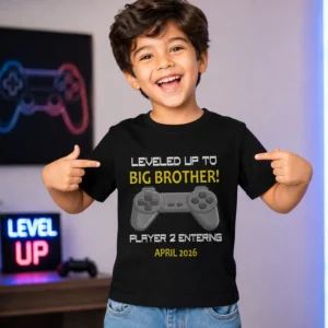 Boy wearing black gaming themed t-shirt with text leveled up to big brother player 2 entering April 2026 for pregnancy announcement