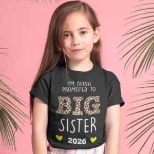 Young girl wearing a black Big Sister 2026 pregnancy announcement t-shirt with leopard print text on a pink background