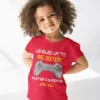 Little girl wearing a red big sister announcement t-shirt with “Player 2 Entering April 2026” gaming design