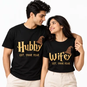 Indian couple wearing matching black Hubby and Wifey T-shirts with gold fantasy-style lettering, brown wizard hat illustrations, and EST. YOUR YEAR text.