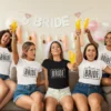 Group of women wearing matching bride and team bride t-shirts celebrating a bachelorette party with drinks and decorations