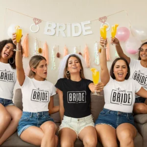 Group of women wearing matching bride and team bride t-shirts celebrating a bachelorette party with drinks and decorations