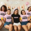 Group of women wearing matching Bride and Team Bride t-shirts at a bachelorette party, sitting together and celebrating with drinks and decorations