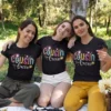 Three women wearing matching black Cousin Crew t-shirts with colorful typography during a picnic outing