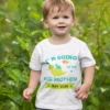 Toddler wearing a personalized big brother announcement T-shirt with cute dinosaur design and due date print outdoors
