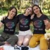 Three women wearing personalized cousin crew Goa trip T-shirts sitting together outdoors, showcasing matching vacation outfits