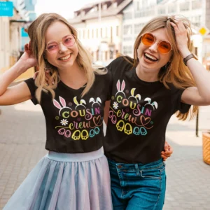 Two young women wearing black personalized Cousin Crew T-shirts with colorful typography design, ideal for family trips and group outfits