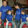 Family of four wearing matching blue personalized vacation t-shirts with 2026 print, sitting together and smiling during a trip