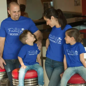 Family of four wearing matching blue personalized vacation t-shirts with 2026 print, sitting together and smiling during a trip