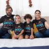 Family of four wearing matching black “Vacay Mode On” personalized vacation T-shirts sitting together, perfect for travel and holiday photos