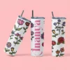 White slim tumbler with colorful floral design and custom name printed vertically, featuring a lid and straw on a pink background
