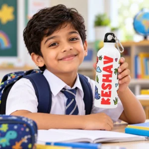 Indian school-age child holding a personalized KESHAV dinosaur aluminum sipper bottle at a classroom desk with school supplies and backpack.