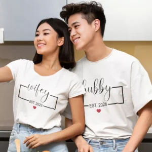 Couple wearing matching white Wifey and Hubby T-shirts with custom year print taking a selfie together