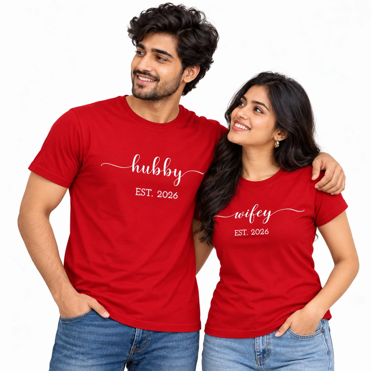 Smiling Indian couple wearing red matching T-shirts with white lowercase hubby and wifey cursive lettering, decorative flourishes, and EST. 2026 prints.