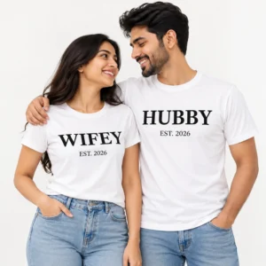 Smiling couple wearing matching white WIFEY and HUBBY T-shirts with bold black serif lettering and EST. 2026 printed beneath each design.