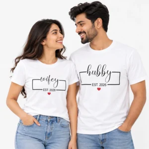 Couple wearing matching white T-shirts with black cursive wifey and hubby lettering, rectangular line frames, EST. 2026 prints, and small red hearts.