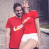 Couple wearing red matching Wifey and Hubby typography T-shirts, smiling together in a romantic outdoor setting