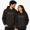 Bride and groom wearing matching black personalized wedding hoodies with custom year text, designed for newlywed couple apparel and wedding gift outfits.