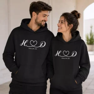 Couple wearing matching black personalized hoodies with initials and a date design, suitable for custom anniversary sweatshirts and matching couple outfits.