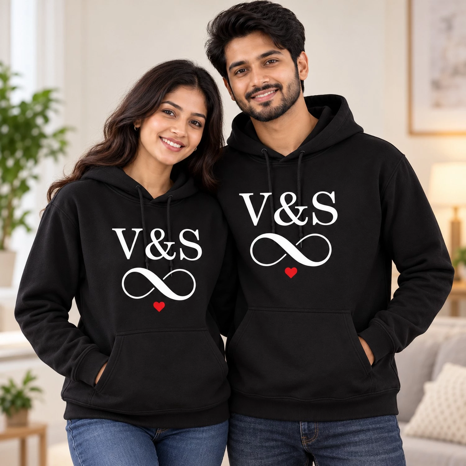 Matching personalized couple hoodie pair in black, modeled by an Indian man and woman, showcasing regular fit with V&S initials and infinity heart print.