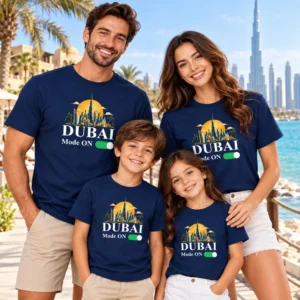 Family of four wearing matching navy blue Dubai Mode ON vacation T-shirts at a beachside resort setting with palm trees and skyline in the background.