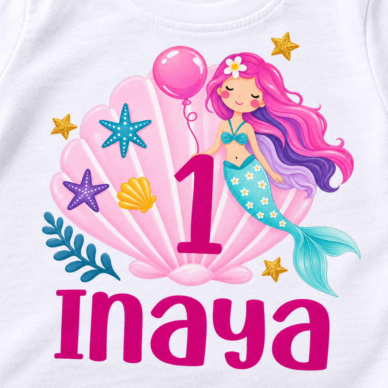Close-up of personalized 1st birthday t-shirt print showing a pink mermaid shell design, number 1, and the name Inaya on white cotton fabric