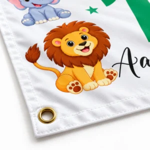 Close-up of personalized kids birthday tapestry corner showing a gold metal grommet, finished fabric edge, stitching, lion artwork, and print detail.