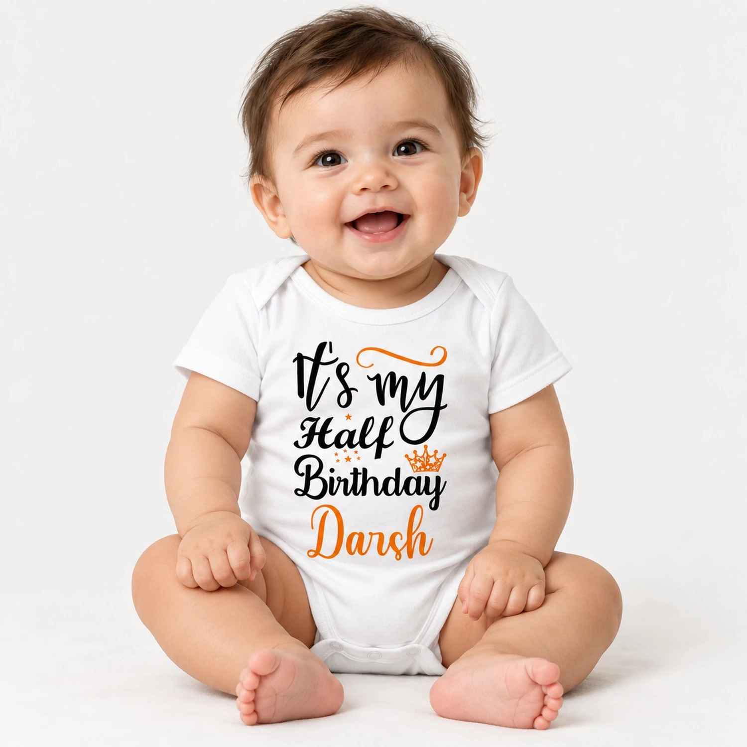 Smiling baby wearing a white personalized half birthday baby romper with black and orange “It’s my Half Birthday Darsh” design.