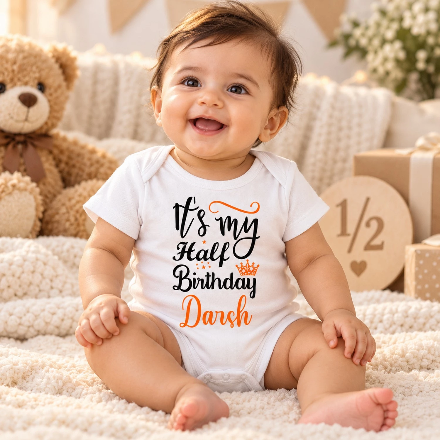 Smiling baby in a white personalized Darsh half birthday romper surrounded by soft birthday props, gifts and a wooden half milestone sign.