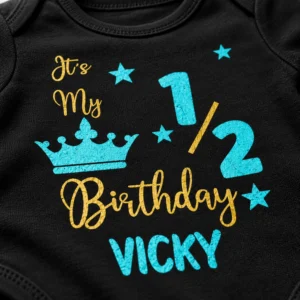 Close-up of the “It’s My 1/2 Birthday VICKY” personalized print on a black baby romper with turquoise crown and stars.