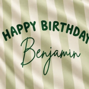 Close-up of sage green and cream personalized birthday tapestry fabric with dark green Happy Birthday and Benjamin printed lettering.