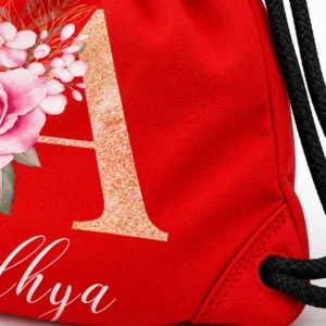 Close-up of a red personalized kids drawstring bag showing woven fabric, black drawstring cord, gathered channel, seams, stitching, and floral print.