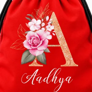 Close-up of the Aadhya personalization on a red kids drawstring bag with a glittery letter A, pink flowers, and white script name.