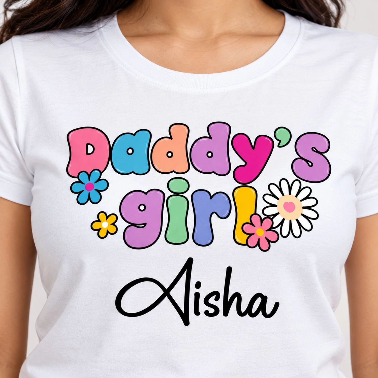 Close-up of a white personalized women's T-shirt showing colorful Daddy's Girl bubble lettering, flower illustrations, and Aisha in black cursive print.